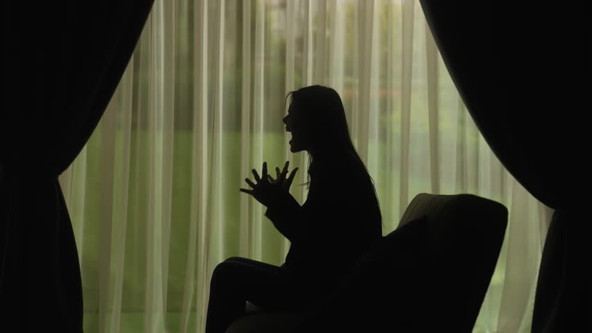 A silhouette of a woman screaming and expressing anger or frustration in front of sheer curtains, conveying emotion and intensity. Mental Health Concept. Slow motion.