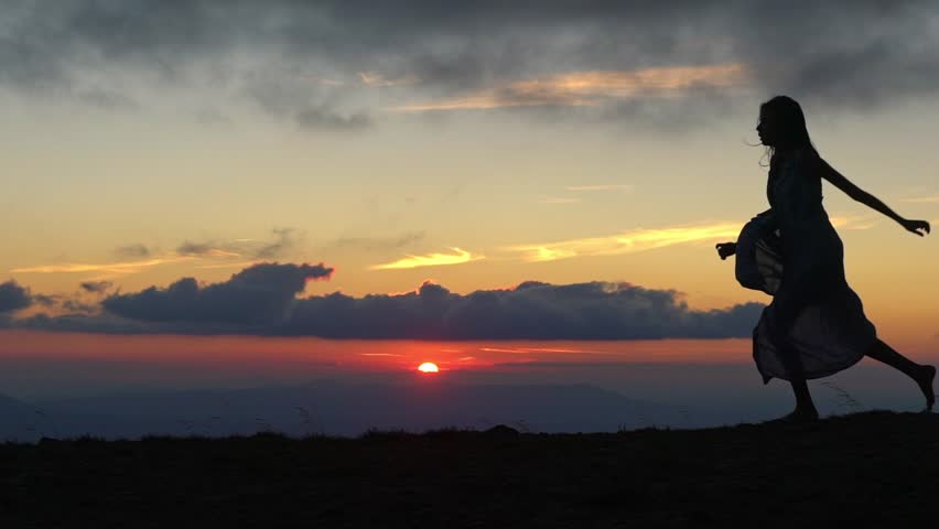 Silhouette of carefree girl jumping in the sunset. Young woman running freely in field. Romantic silhouette of a girl at sunrise. Happy woman enjoying the wind outdoors. Tourist traveler jump on sky.