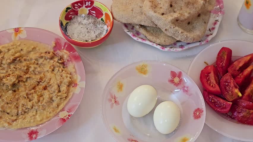 Egyptian breakfast of a plate of mashed fava beans mixed with oil, sesame tahini, cumin, spices, traditional popular street Egyptian fava bean, boiled eggs, flat bread, sliced tomatoes and salt
