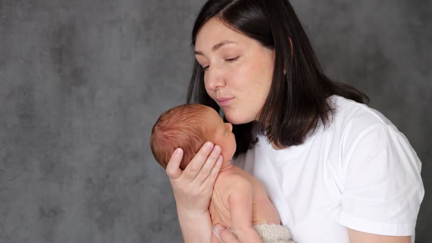 Mother gently kisses forehead of newborn baby boy in arms. Profound sense of love and adoration with woman eyes closed in evident affection