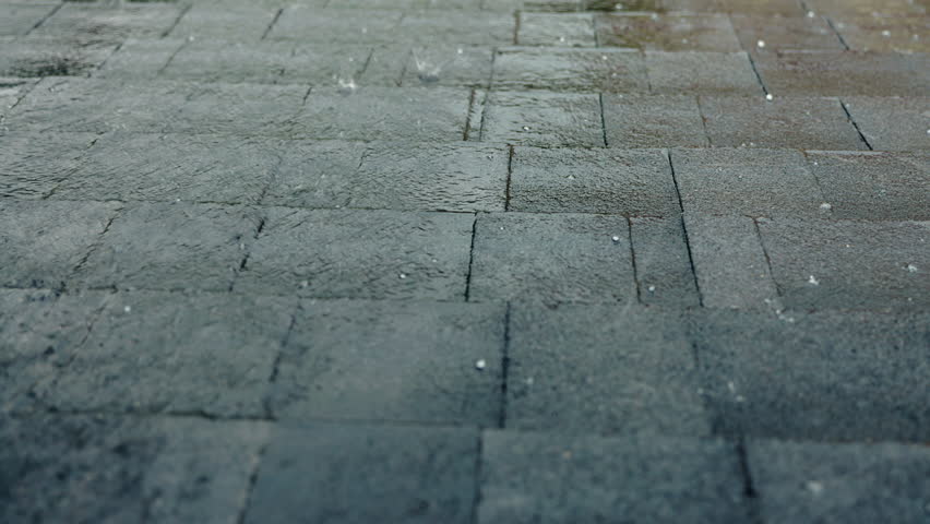 Heavy rain and hail falling on a roof covered with asphalt shingles, showing durable roofing materials protecting against severe weather. High quality 4k footage