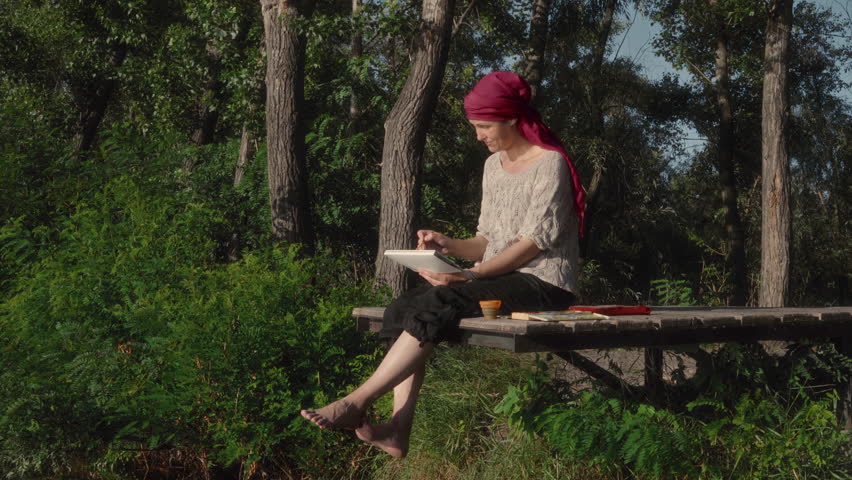 Female artist painting a river landscape in watercolor while sitting on a wooden pier