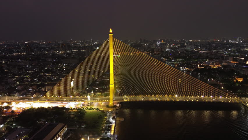 Aerial view of illuminated Rama VIII Bridge at night. Cable-stayed bridge crossing Chao Phraya River in Bangkok, Thailand, 4k