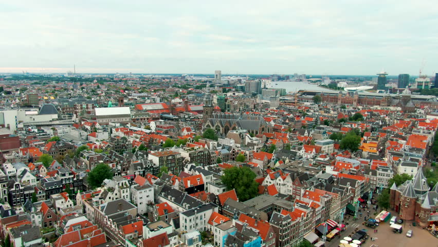 Drone shot over Amsterdam city center with Oude Kerk, traditional Dutch architecture, red roofs, and canal layout. Perfect for travel, tourism, and urban heritage content. 4K establishing aerial view