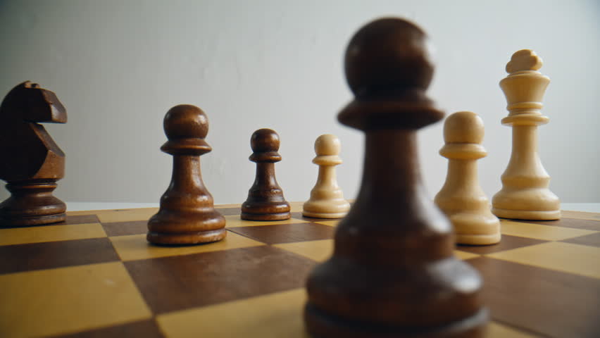 Closeup of man hand moving brown pawn piece on chess board. Person playing logic game. Fingers lifting unit on battlefield filled with different figures. Leadership and business strategy concept 