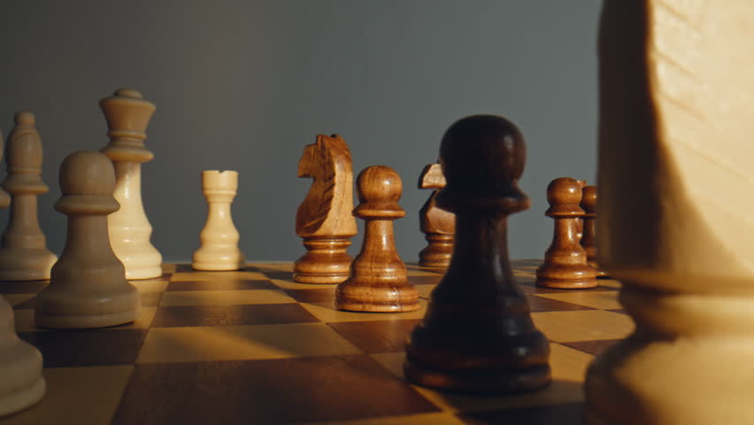 Fingers lifting pale pawn on battlefield filled with mahogany figures closeup. Scene expresses calculation bold initiative quick judgment mental strength and clarity under high tension match condition