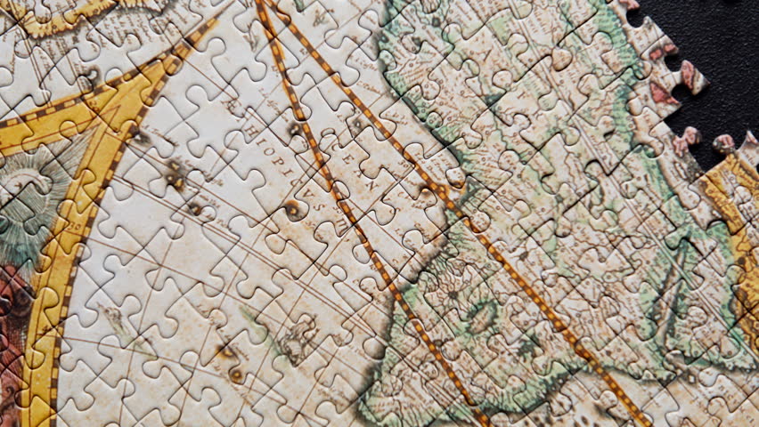 Incomplete world map puzzle lying over dark background forming structure closeup. Vintage brain teaser picture. Historical landscape details fragmented yet coming together. Jigsaw assembling on black