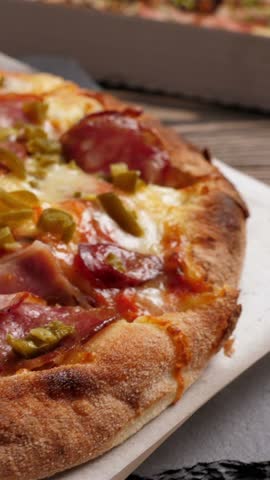 One salami and bacon pizza on black slate platter rotating, closeup. Vertical footage