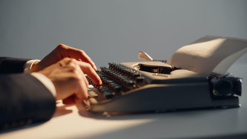 Fingers pressing old-fashioned keys in bright sunlight closeup. Unrecognizable author composing book pages on classic dark manual typewriter stationed at workspace. Mysterious writer developing novel