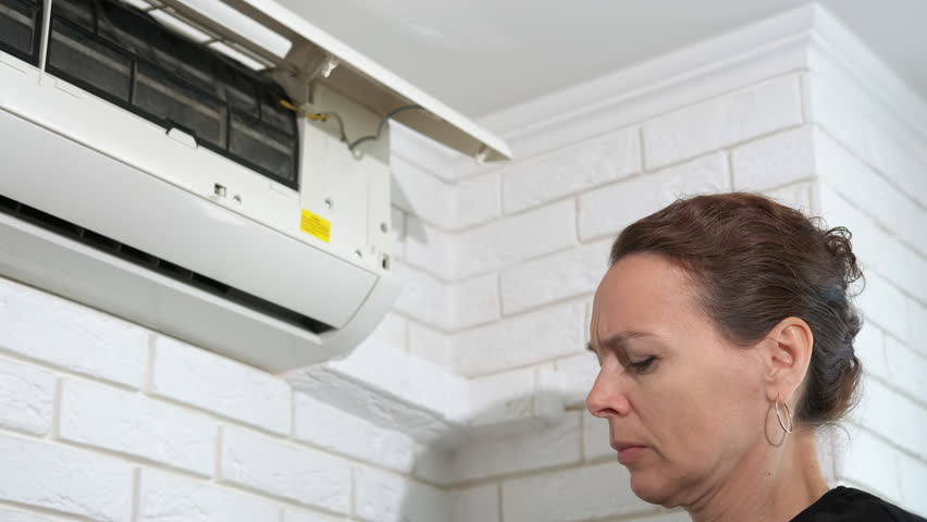 Woman by broken conditioner indoor. A view of frustrated female try to open the air conditioner from the wall indoor.