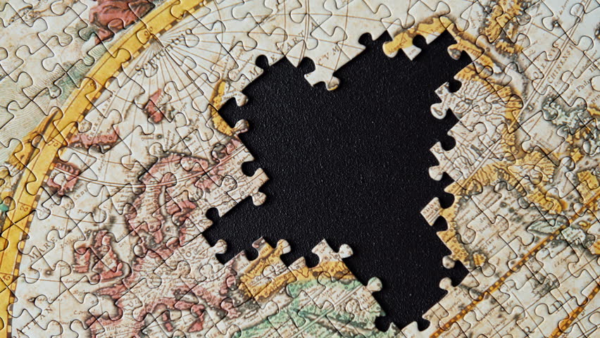 Fingers placing cardboard segment gently on surface assembling classic puzzle closeup. Old styled world layout forming slowly on dark table. Person positioning element connecting geography shapes