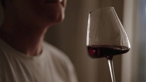 Young man in white t-shirt savoring glass of red wine at home. Close-up of male sommelier enjoying red wine, sunlight illuminating deep crimson color while gracefully sipping beverage, slow motion. - Powered by Shutterstock - Get 15% off with code: PIKWIZARD15