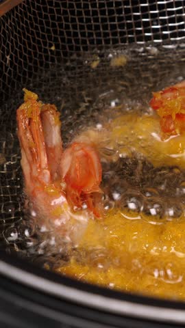 Cooking tempura shrimps in deep fryer. Closeup. Vertical footage
