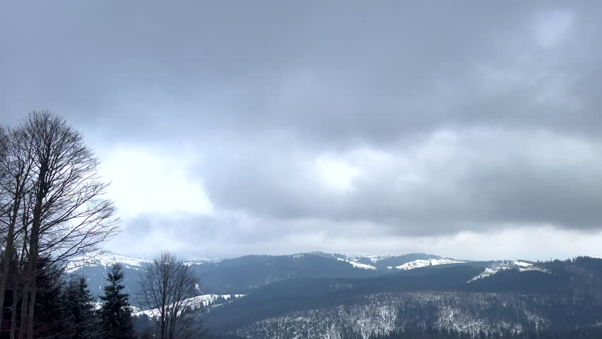 Beautiful winter landscape with snow covered hills and forests under moving clouds