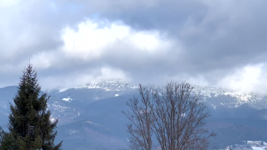 Clouds moving above snowy mountain peaks and trees