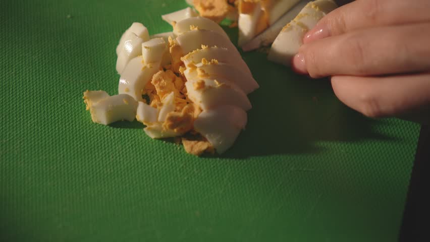 Sliced boiled egg on green cutting board with hand in frame