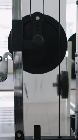 Close-up view of gym equipment next to weights and swivel cables in a brightly lit gym