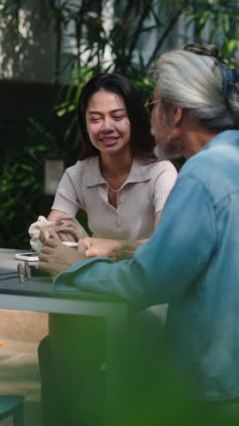 Young Asian woman sitting with her old white-haired father outdoors together on a quiet terrace