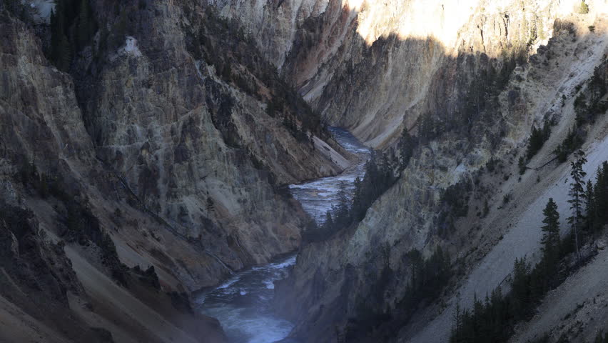 Grand Canyon of the Yellowstone, medium shot from Brink of Lower Falls on a summer evening, featuring the Yellowstone River and colorful canyon walls glowing in warm light and deep shadows.