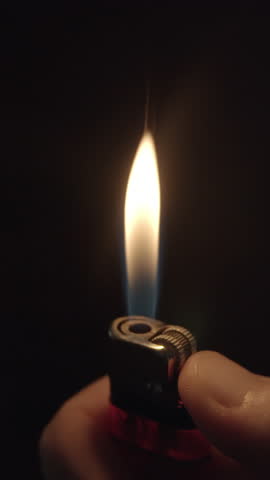 Vertical close-up of thumb slowly igniting metal lighter in darkness — ideal for product intros, moody branding or mobile ad transitions.