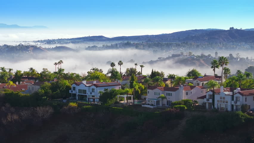 Experience stunning aerial views of Calabasas, California in the early morning, highlighting misty hills and luxury homes under a vibrant blue sky, creating a tranquil and picturesque landscape