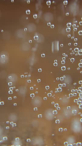 Effervescent carbonated water displays dynamic bubble patterns with intensive gas formations ascending through amber-tinted liquid creating hypnotic visual movement for relaxation content