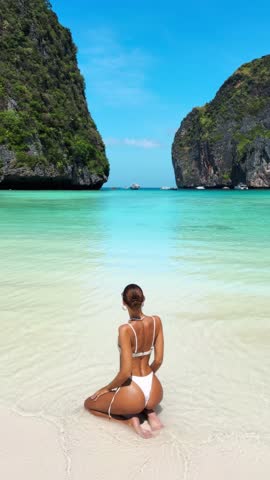 Cheerful female model poses playfully in a white bikini on the shore of Maya Bay, Thailand. Fun, high quality tropical beach video ideal for travel, beauty and influencer promotions.