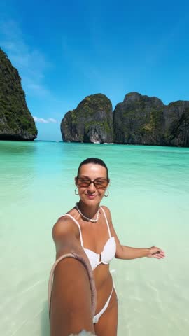 Confident young woman taking selfies in the crystal clear waters of Maya Bay, Phi Phi Islands, Thailand. Ideal for travel, influencer, social media, and luxury summer lifestyle videos.