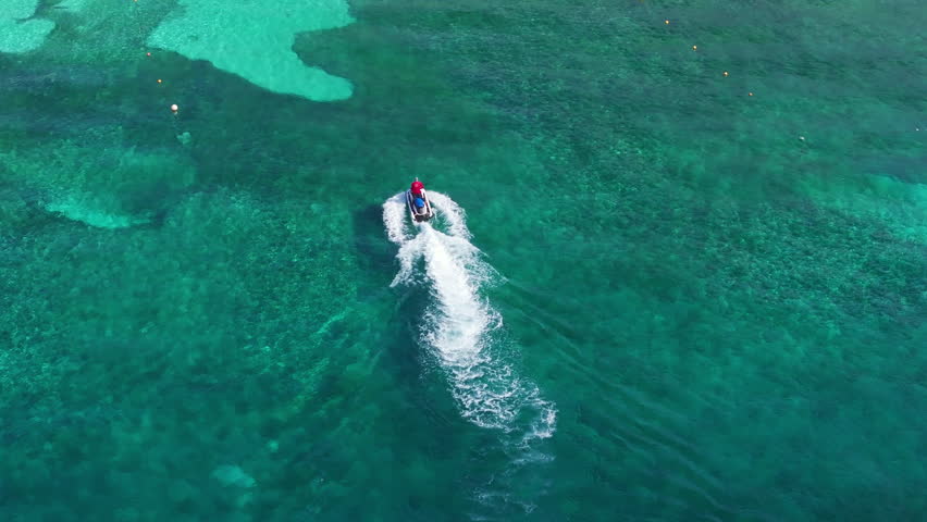 Witness the beautiful turquoise waters of Cozumel, Mexico, with vibrant coral reefs, as a jet ski glides swiftly through the inviting ocean in this breathtaking aerial view of a tropical paradise