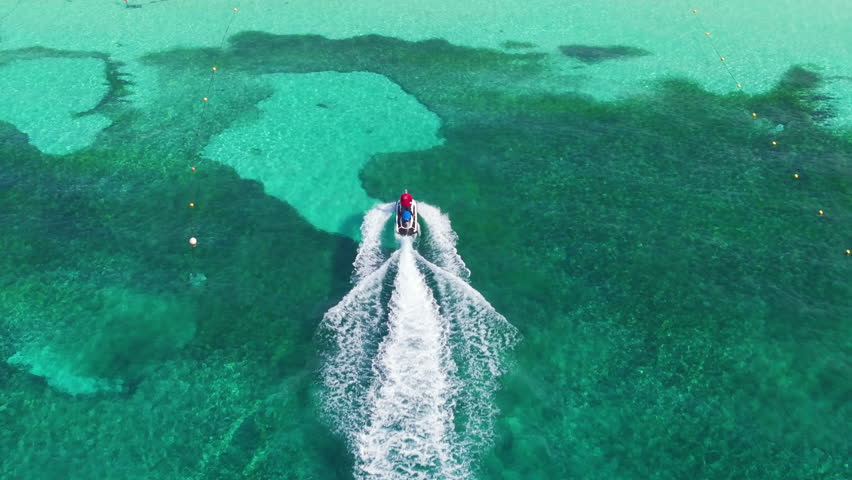 Witness the beautiful turquoise waters of Cozumel, Mexico, with vibrant coral reefs, as a jet ski glides swiftly through the inviting ocean in this breathtaking aerial view of a tropical paradise