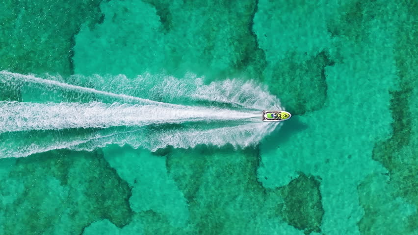 Aerial footage shows a skilled jet ski rider expertly maneuvering sharp turns in the vibrant turquoise waters of Cozumel, Mexico, highlighting the breathtaking Caribbean landscapes around