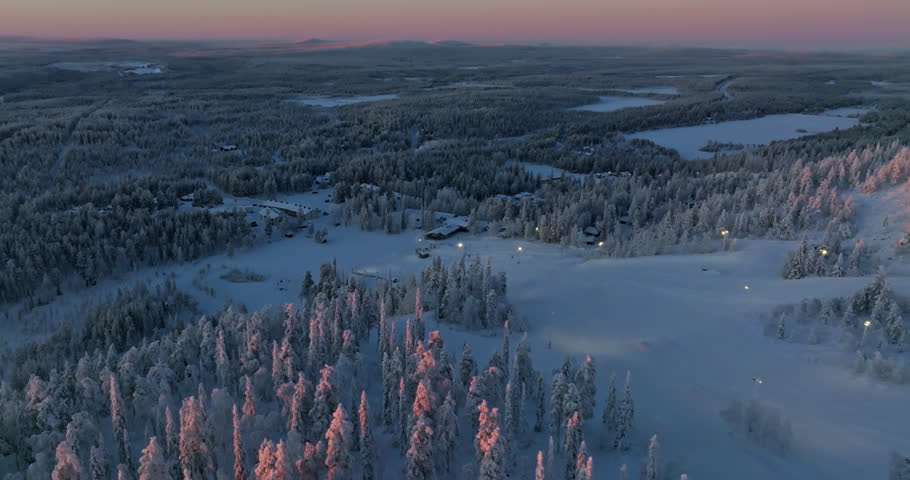 Panoramic aerial around sunlit trees and the slopes of Salla, winter in Lapland