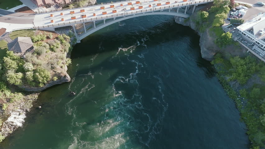Overhead view of a white bridge crossing a river in downtown Spokane, next to a historic red-brick building.