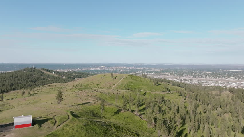 Aerial view of grassy rolling hills near Spokane with distant views of the city skyline under blue skies.