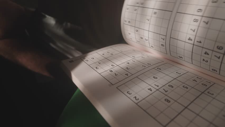Person in sunlit shadowy room flicks through Soduku puzzle book pages