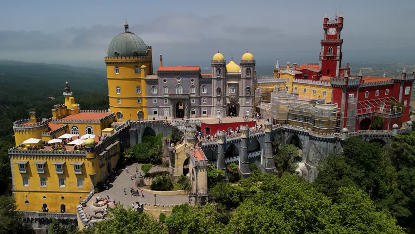 Drone orbits pulls back ascending, unveiling Sintra’s vibrant Palácio Nacional da Pena atop forested hills