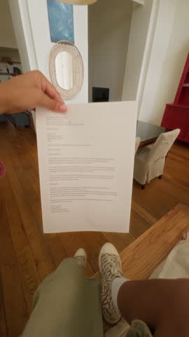 Vertical UGC footage of happy gen Z African American girl opening envelope getting university offer while vlogging on camera of smartphone at home