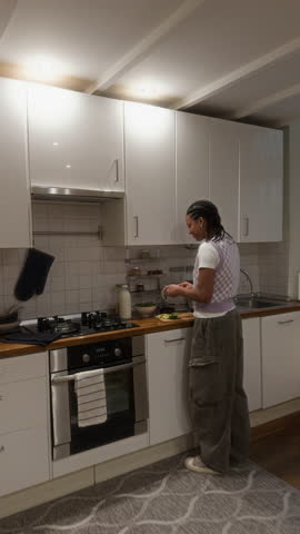 Vertical shot of young African American mom vlogging as daughter peeling avocado cooking at home kitchen and communicating, UGC