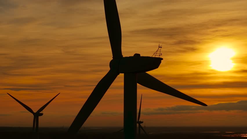 Windmill spinning in golden sky. Creating power with smooth breeze. Generating electricity from turning blades. Delivering renewable energy using environmental flow