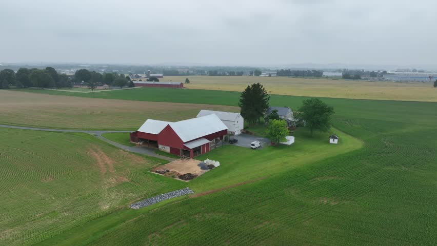 Aerial view of tranquil farm surrounded by lush green fields. classic red barn, farmhouse and open landscapes, capturing the essence of rural life and agriculture. Rainy day in Pennsylvania.