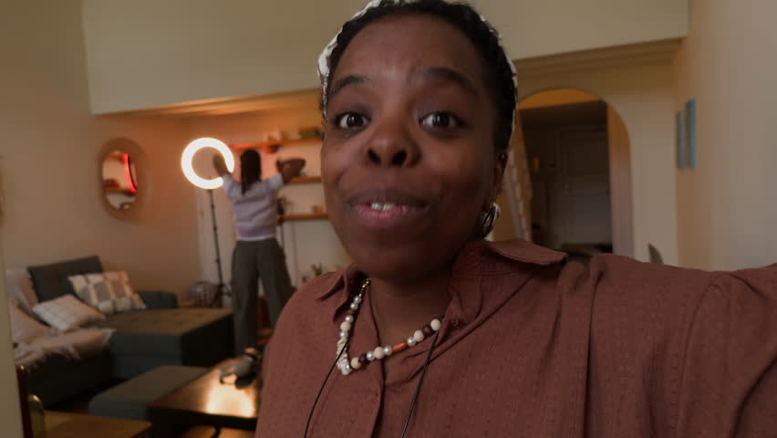 UGC of young African American woman talking on camera, vlogging at home while teenage daughter practicing dance by ring light
