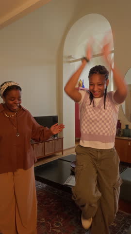 Vertical UGC footage of young black woman repeating dance moves after gen Z teenage daughter vlogging on camera at home