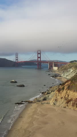 Flock Of Birds Flying Over Golden Gate Bridge With Fog From Baker Beach In San Francisco, California, USA. - aerial vertical shot