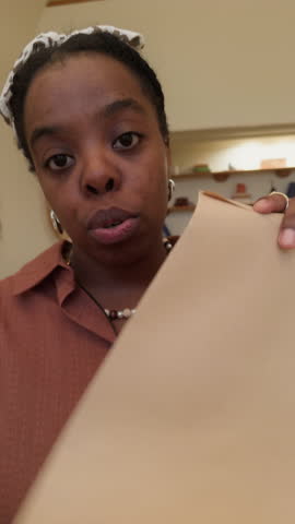 Vertical UGC footage of upset black woman vlogging on camera opening envelope with past due bill and touching forehead in stress at home