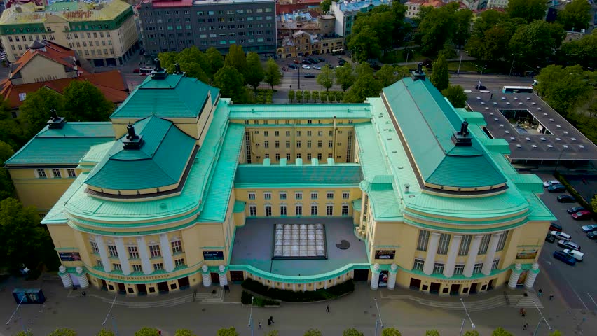 Gorgeous aerial drone revealing shot of a large yellow colored theatre that is an Estonian national Opera house during a cloudy day in Tallinn central citty with medieval buildings and Baltic sea seen