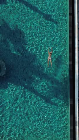 Top view of mid adult woman swimming in pool under the palm trees at sunny day.Bali.Indonesia.Vertical video