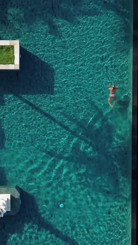 Top view of mid adult woman swimming in pool under the palm trees at sunny day.Bali.Indonesia.Vertical video