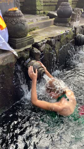Close-up of woman performing traditional water purification ritual at the temple in Ubud Bali, Indonesia. Spiritual moment ideal for religion, culture, and travel content.