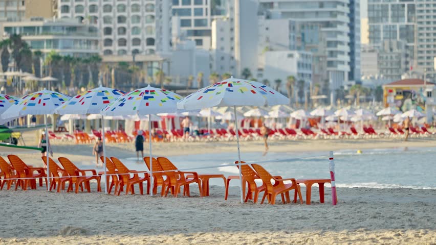 Colorful plastic beach chairs and tables with sun umbrellas in Tel Aviv beach. Early morning in summer season as people enjoy a swim in mediterranean sea or jog on sandy shore in Israel famous city