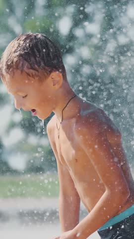 Boy of seven years having fun, bathes in a fountain and playing water splash in outside, on a hot summer day. Slow motion